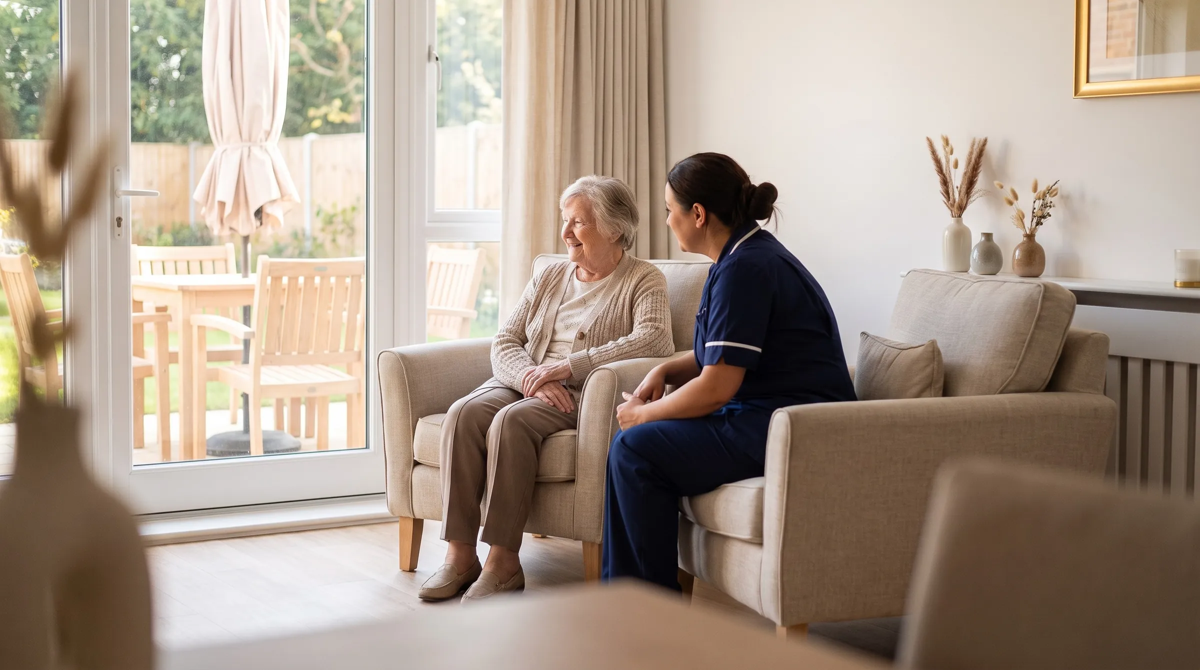 A carer and an older resident sharing a conversation in a sunlit lounge